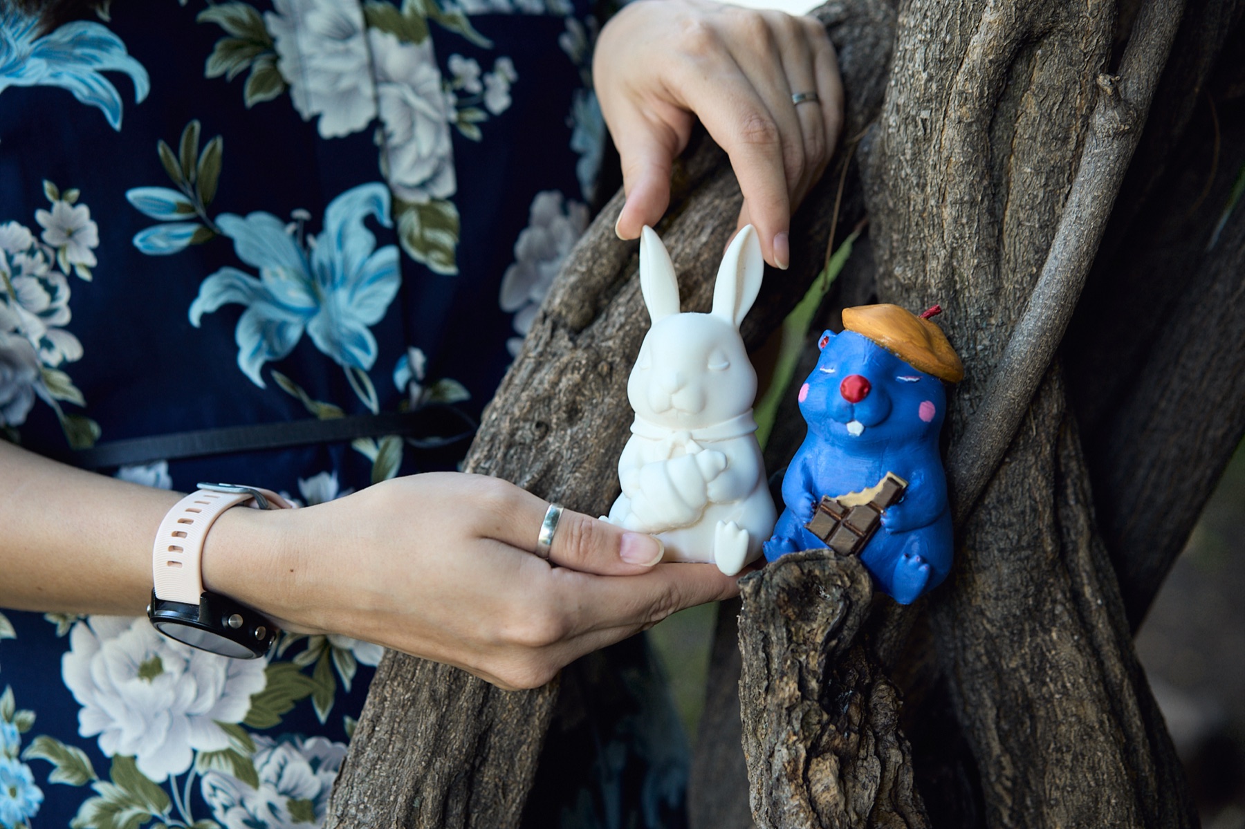 Hands presenting Colette the white bunny beside Otto the blue beaver in a tree
